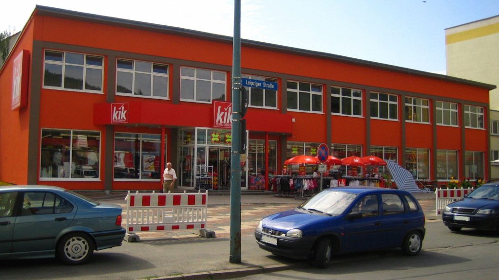 Im Hintergrund das rote Gebäude des "kik" am Emil-Höllein-Platz 1. Im Vordergrund der Platz, Gehweg und ein Stück der Straße.