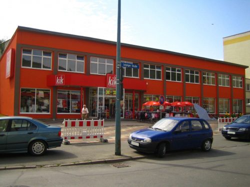 Zu sehen der Emil-Höllein-Platz 1, im Hintergrund das rote Gebäude mit dem Händler "kik", im Vordergrund die Straße und Gehweg.