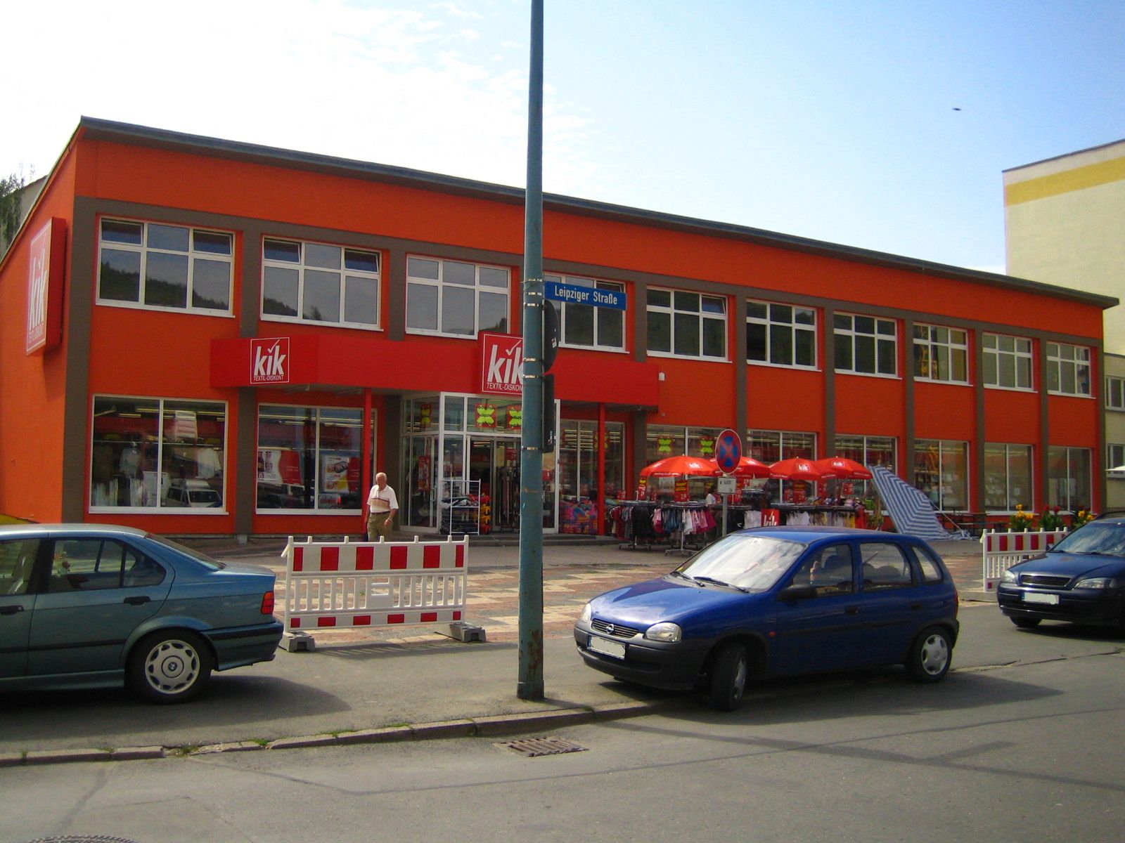 Im Hintergrund das rote Gebäude des "kik" am Emil-Höllein-Platz 1. Im Vordergrund der Platz, Gehweg und ein Stück der Straße.