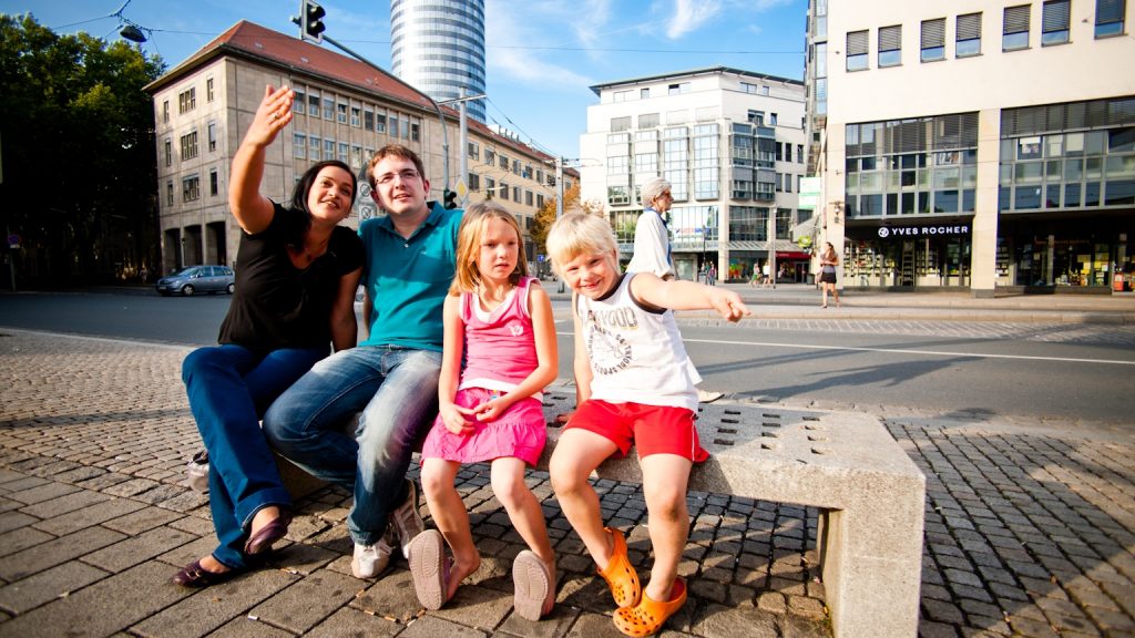 Freundliche Famile winkt, im Hintergrund ist der Intershoptower in Jena zu sehen.
