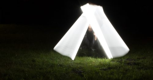 Fotografie einer Person mit Leuchtstoffröhre, die mit dem Licht ein Zelt um sich herum nachbildet