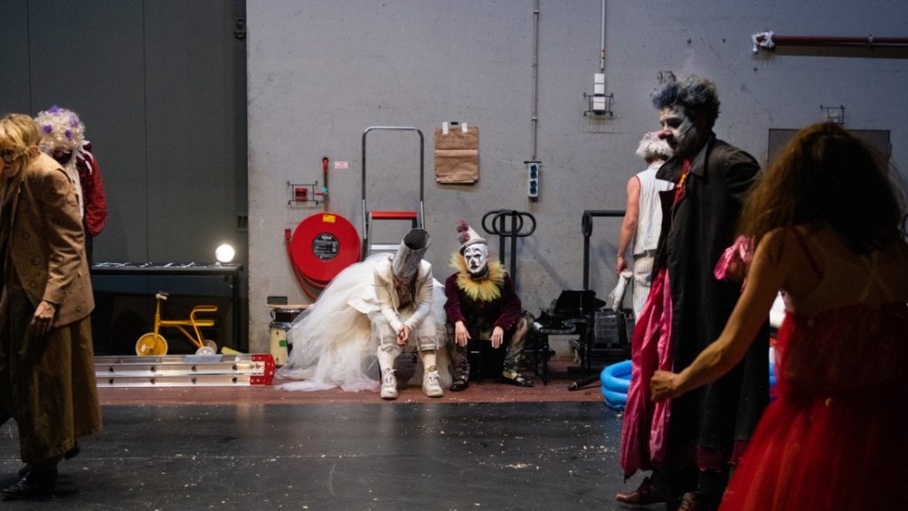 Szene aus der Vorstellung "Der Clowns-Kongress": Clowns sitzen und stehen erschöpft hinter der Bühne