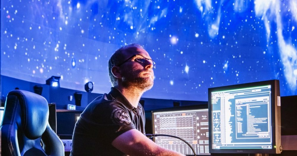 Stefan Harnisch an seinen Rechnern im Planetarium mit projiziertem Sternenhimmel