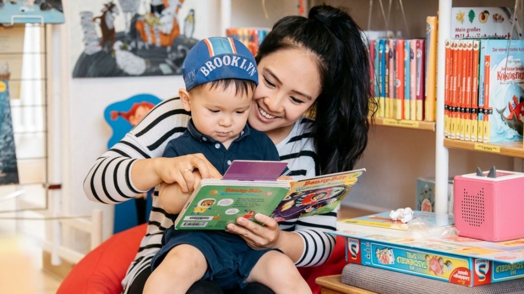 Frau und Kind mit asiatischem Äußeren in der Stadtteilbibliothek Lobeda schauen sich ein Kinderbuch an