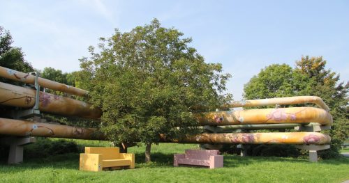 Gelbes und rosafarbenes Sofa neben einem Baum, der vor den bunt bemalten Fernwärmetrassen WohnZimmer" in Jena steht
