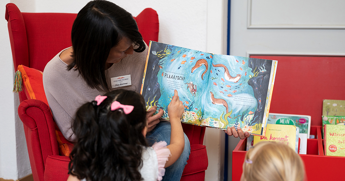 Mädchen schauen sich zusammen mit einer Kollegin der EAB Jena ein Kinderbuch an