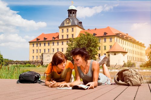 Das Schloß Zeitz im Hintergrund, im Vorgergrund liegenb das Frauen auf einem Podest und blättern im Reiseführer