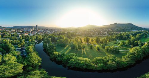 Blick auf Jena, von oben, ins grüne, auf die Saale, im Hintergrund die Berge und links die Lichtstadt Jena, die Sonne geht gerade auf