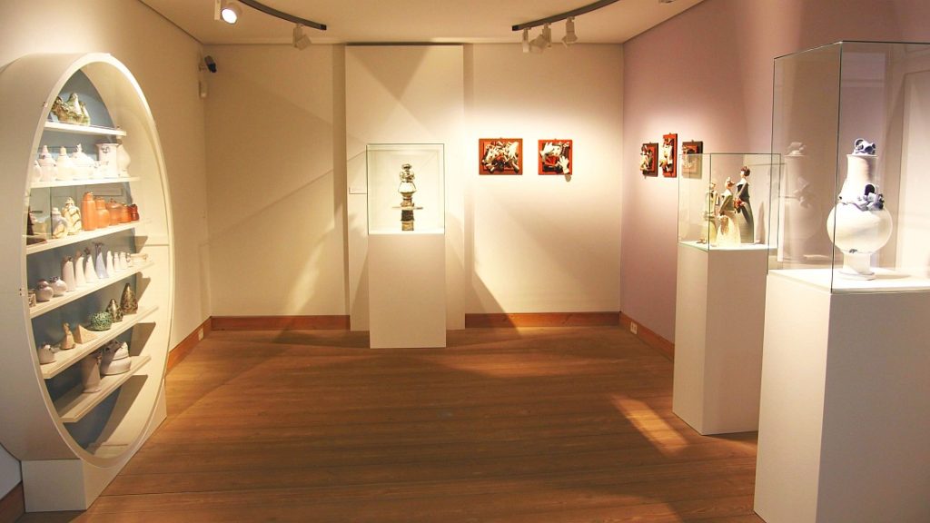 Blick in die Ausstellung von Ulli Wittich-Großkurth im Stadtmuseum Jena mit verschiedenen Keramikarbeiten in Vitrinen und Regalen, z. B. Vasen und Figuren