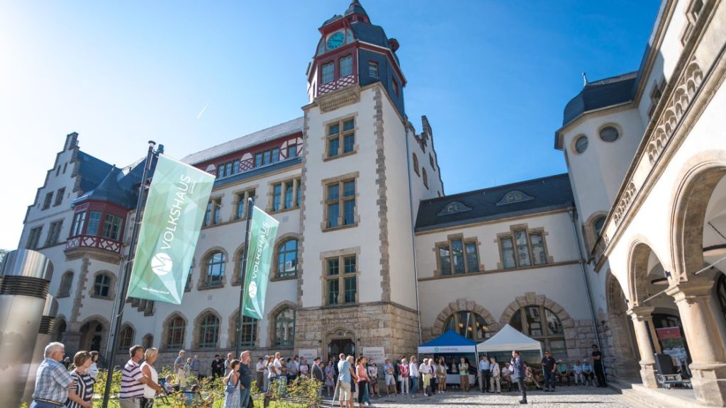Oberbürgermeister hält eine Rede auf dem Vorplatz mit Pavillons und Besucher:innen beim Tag der offenen Tür im Volkshaus Jena