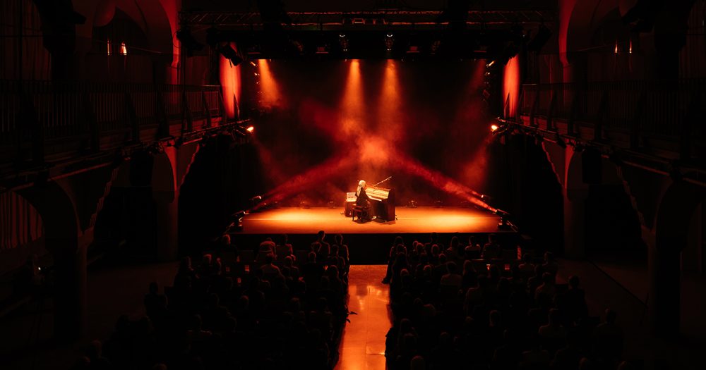 Pianistin auf der Bühne des Volksbads Jena in atmosphärischem orangefarbenen Licht bei ArenAkustik