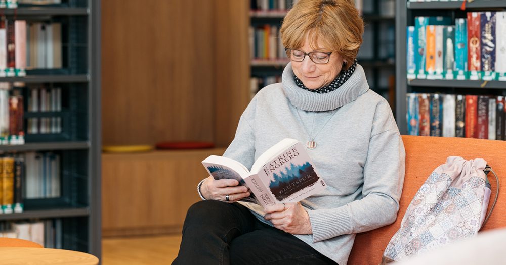 Eine Frau sitzt in einer gemütlichen Ecke der Ernst-Abbe-Bücherei Jena und liest ein Buch