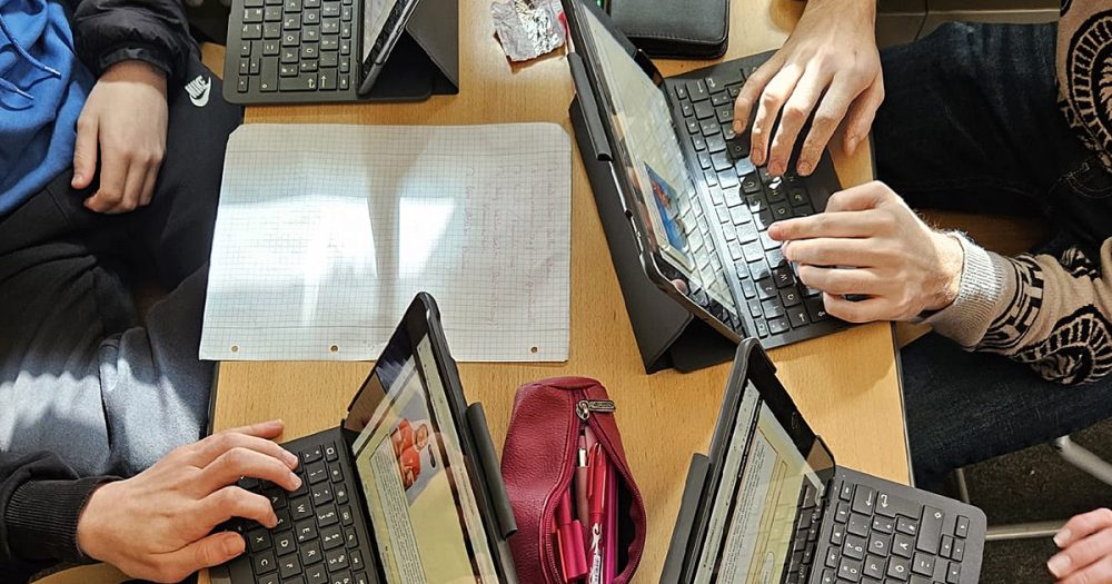 Sicht auf einen kleinen Tisch, an dem vier Mensche ndicht gedrängt mit ihren Laptops und Schreibmaterialien sitzen und arbeiten