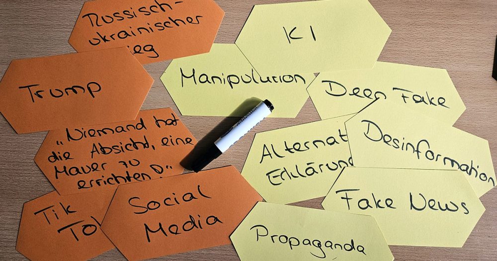 Orangene und gelbe Moderationskarten auf denen Begriffe stehen wie "Fake News", "Deep Fake", "Manipulation", "KI", "Social Media", "Trump" und andere