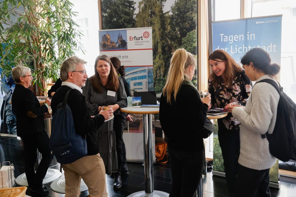 Stand von Jena Convention, an dem Interessierte ins Gespräch kommen, im Hintergrund weisen Rollups auf Jena als Tagungsort hin.