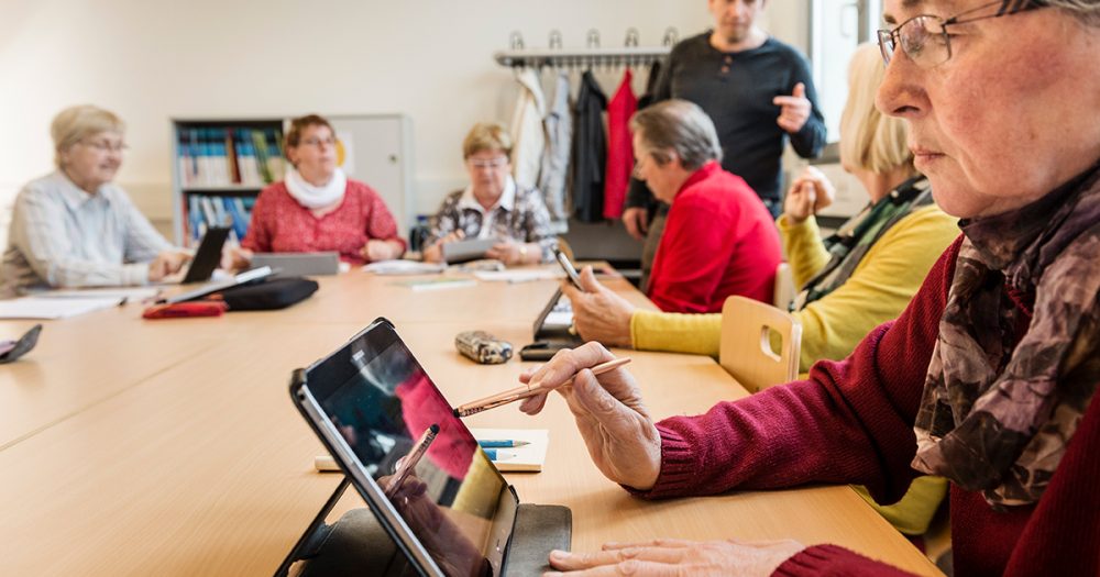 Senior:innen in einem Kursraum der vhs Jena arbeiten an Tablets und Smartphones