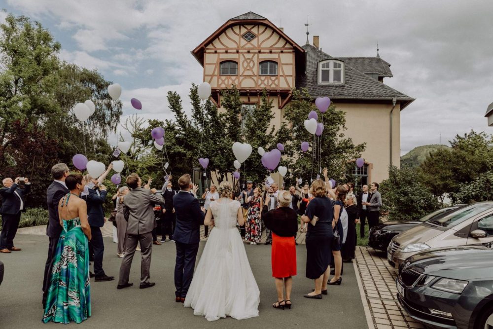 Brautpaar und Hochzeitsgäste stehen vor der Villa Rosenthal und lassen Helium-Ballons in Herzform steigen