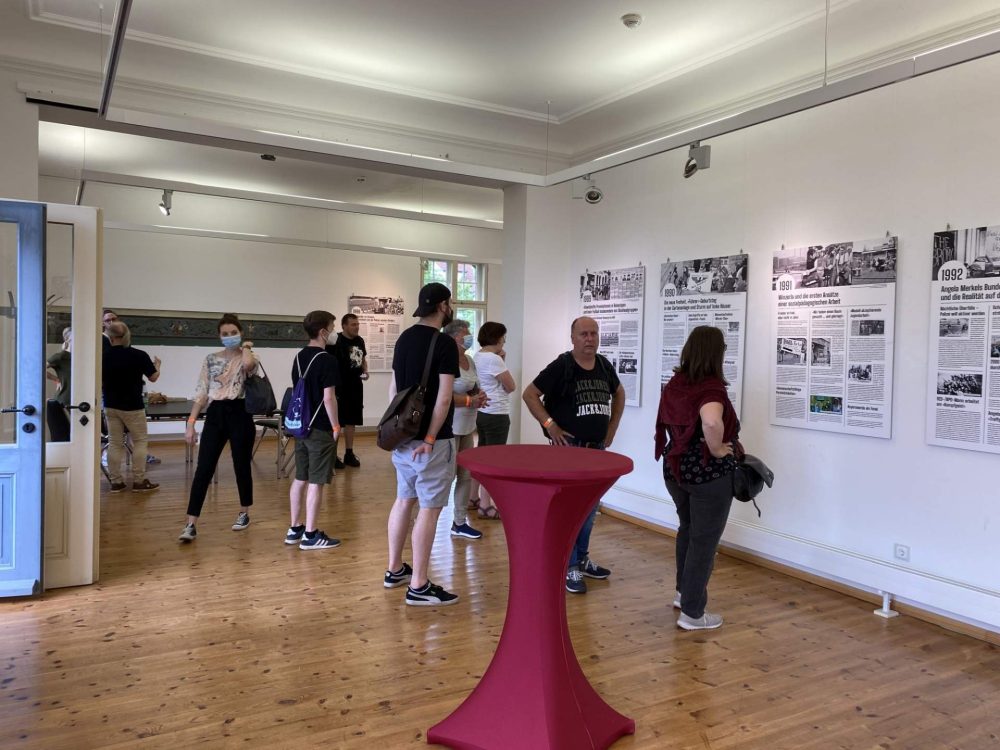 Menschen stehen im Ausstellungsraum der Villa Rosenthal und schauen sich Tafeln an der Wand an.