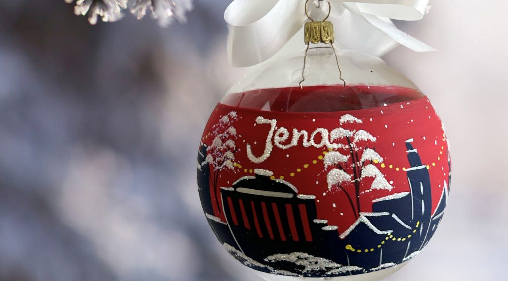 Mit der Skyline der Stadt Jena bemalte rote Weihnachtskugel, welche an einem frostigen Tannenzweig hängt.