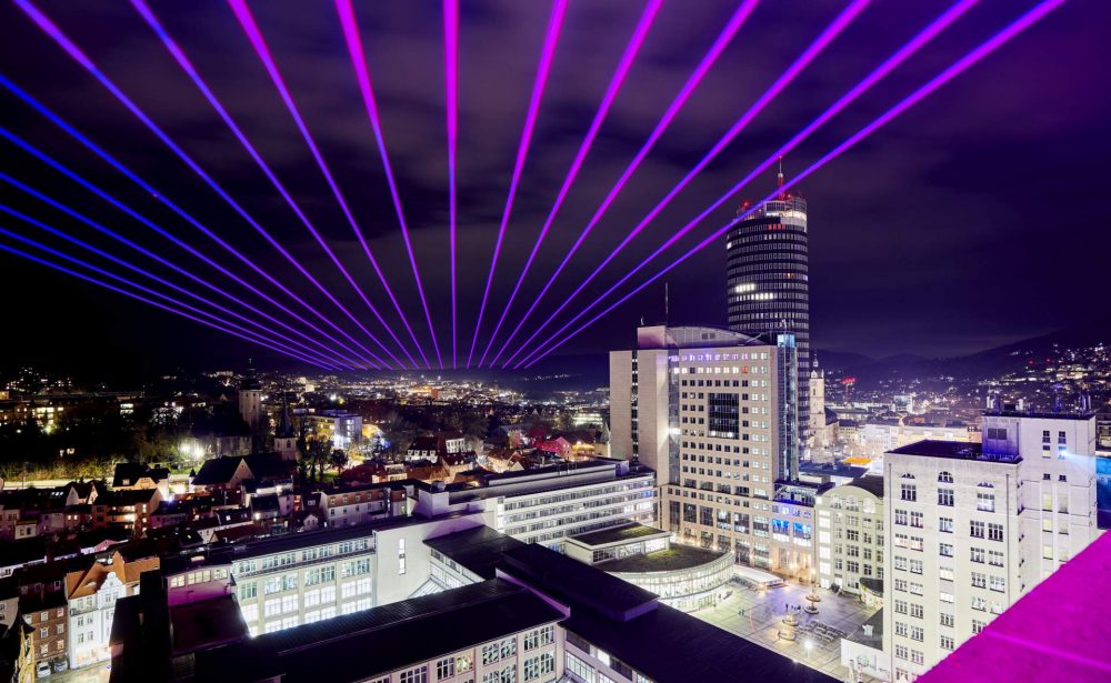 Blau-pinkene Laserstrahlen leuchten über der Innenstadt Jena mit Sciht auf Jentower, Ernst-Abbe-Hochhaus, Unicampus