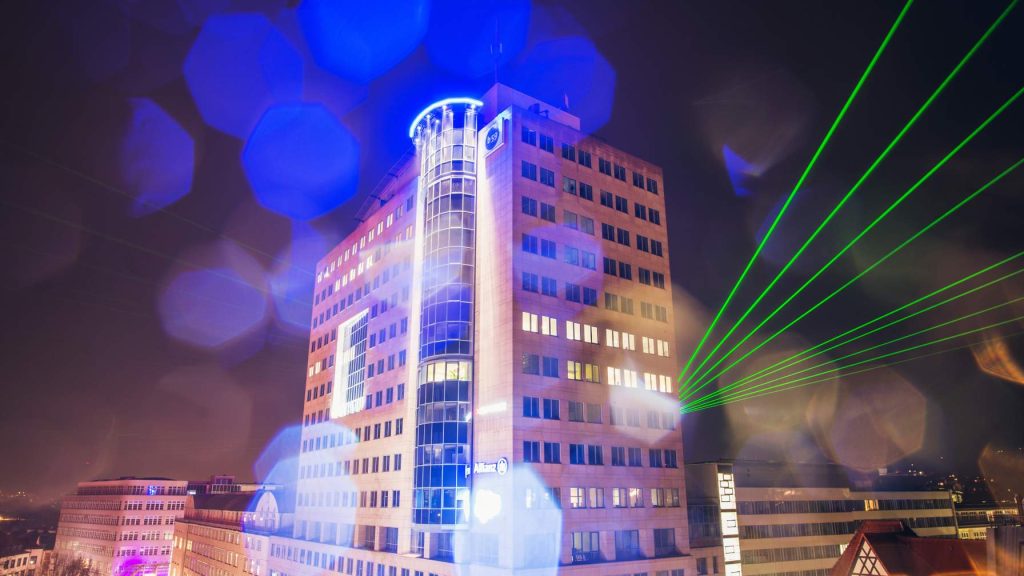 Hochhaus von Ernst-Abbe in Jena, dahinter ragen grüne Laserstrahlen hervor, bei Nacht