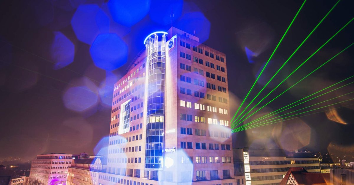 Hochhaus von Ernst-Abbe in Jena, dahinter ragen grüne Laserstrahlen hervor, bei Nacht