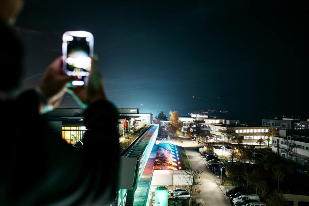 Eine Person macht mit seinem Smartphone ein Bild von der beleuchteten Stadt Jena zur Langen Nacht der Wissenschaften