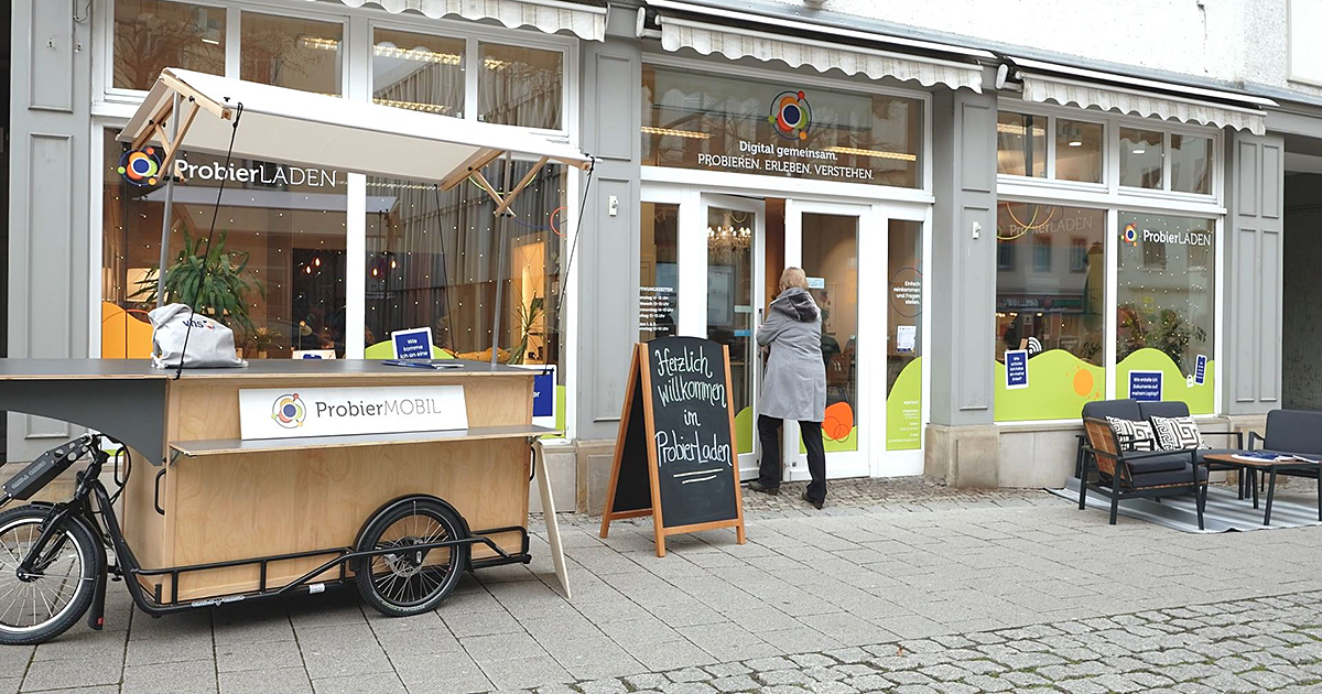 Frau betritt den ProbierLaden Jena, davor steht das ProbierMobil und ein Willkommen-Aufsteller