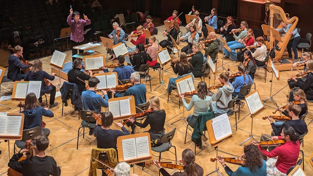 Die erste gemeinsame tutti pro-Probe im Volkshaus Jena, viele Musiker:innen sitzen auf der Bühne mit Ihrem Instrument