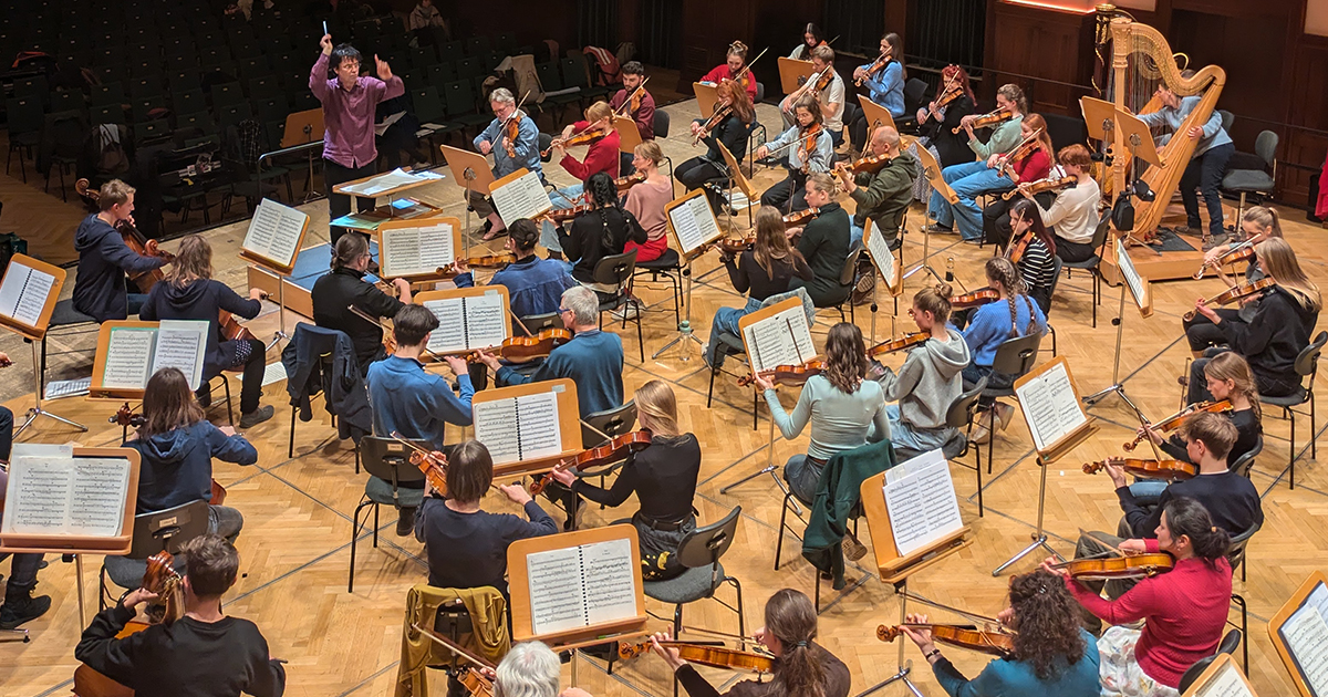 Die erste gemeinsame tutti pro-Probe im Volkshaus Jena, viele Musiker:innen sitzen auf der Bühne mit Ihrem Instrument