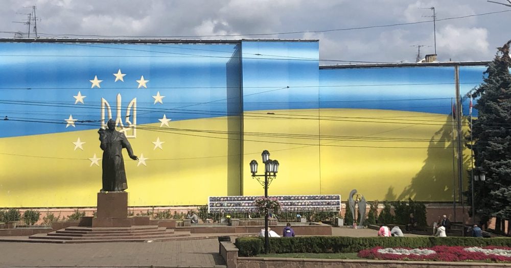 Ein Platz mit einer Statue und parkähnlichen Beeten, gelegen an einem Gebäude mit ukrainischen Farben.