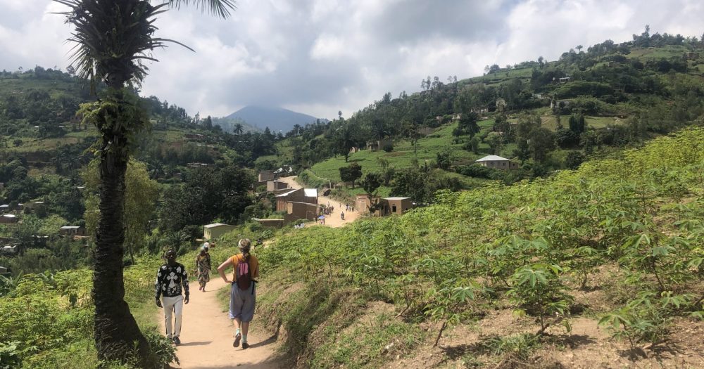 3 Menschen bewegen sich auf einem Weg, der durch Plantagen in Burundi durchführt.