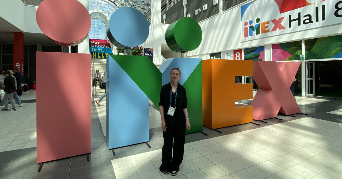 Die JenaKultur-Auszubildende Luise Büttner vor dem IMEX Logo auf der Messe