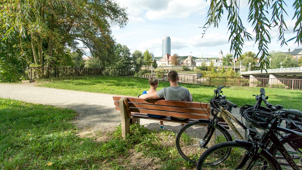 Ein Pärchgen auf einer Bank im Paradiespark Jena mit Blick aiuf dne JenTower und die Räder im Bild