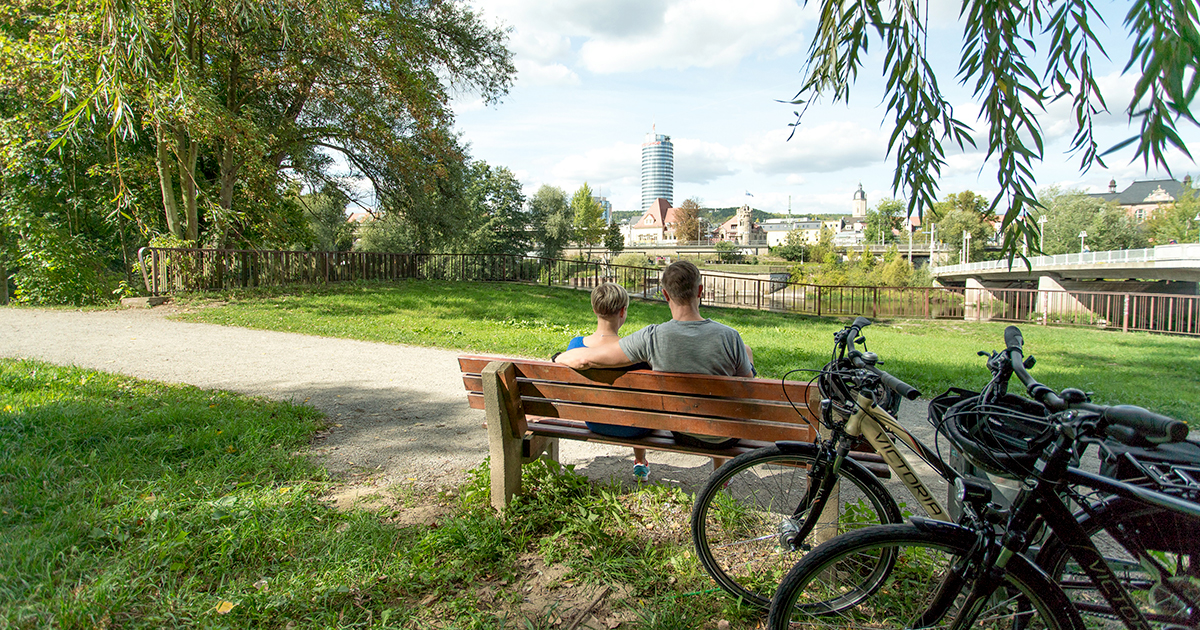 Ein Pärchgen auf einer Bank im Paradiespark Jena mit Blick aiuf dne JenTower und die Räder im Bild