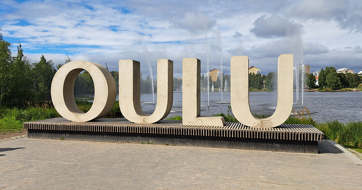 Der Schriftzug "Oulu" in großen Betonbuchstaben vor einem See mit Fontainen
