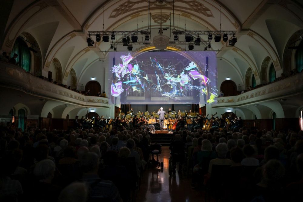 Blick auf die Bühne im Volkshaus Jena mit Orchester und Lichtkunst im Hintergrund