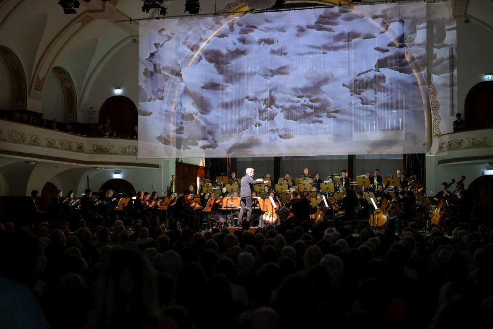 Blick auf die Bühne im Volkshaus Jena mit Orchester und Lichtkunst im Hintergrund