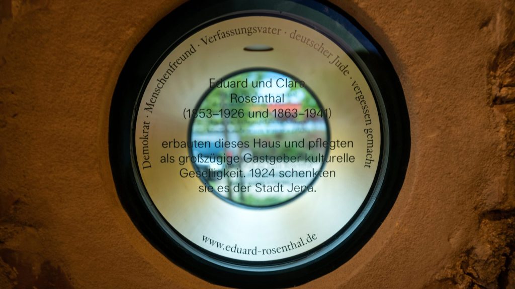 Ein Loch in einer Häuserwand, das mit Glas versehen ist, auf dem die Namen Eduard und Clara Rosenthal stehen und somit ein Denkmal für diese beiden bilden.