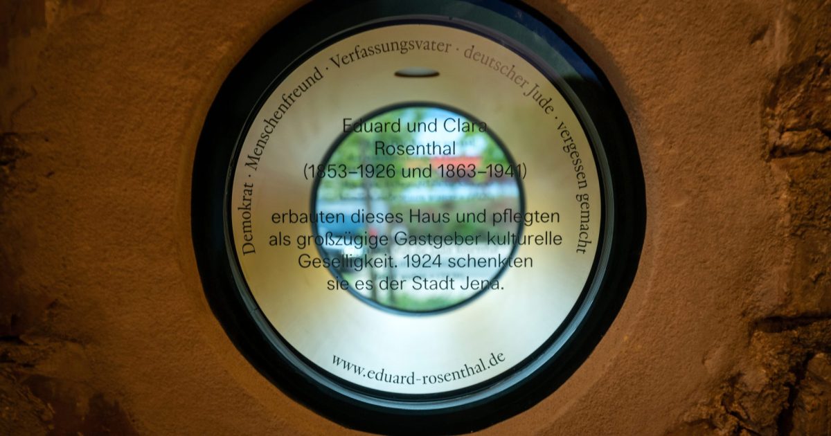 Ein Loch in einer Häuserwand, das mit Glas versehen ist, auf dem die Namen Eduard und Clara Rosenthal stehen und somit ein Denkmal für diese beiden bilden.
