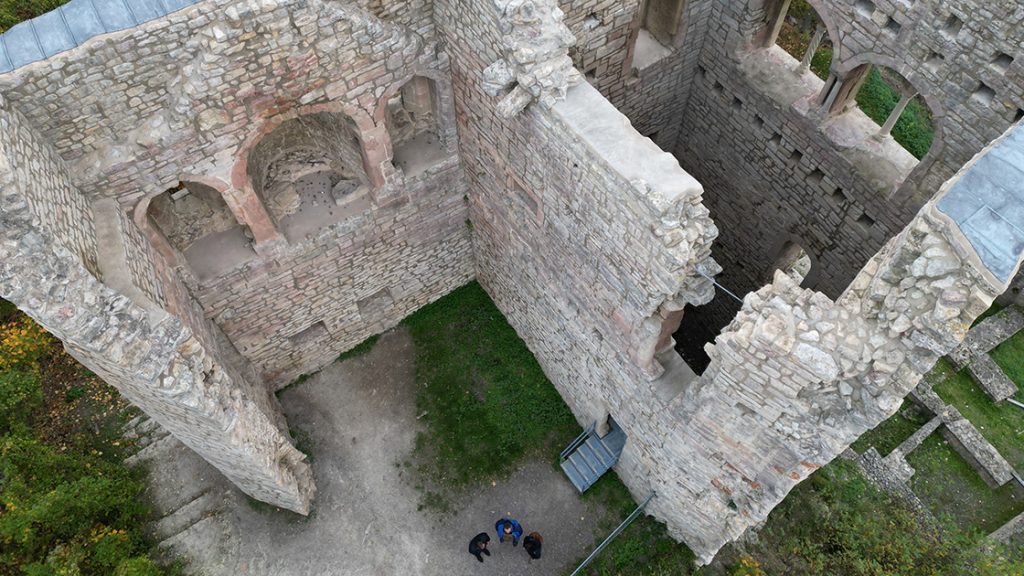 Aufnahme von oben auf die sanierte Lobdeburg, deren Mauern mit Metallschindeln gedeckt ist, daneben stehen Menschen.