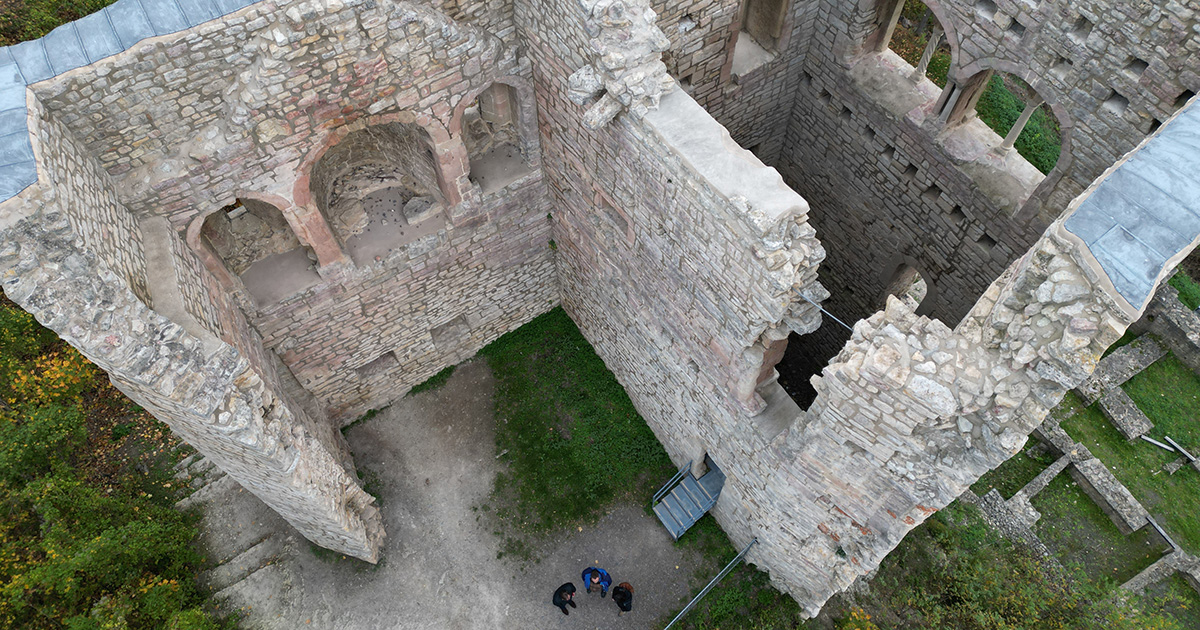 Aufnahme von oben auf die sanierte Lobdeburg, deren Mauern mit Metallschindeln gedeckt ist, daneben stehen Menschen.