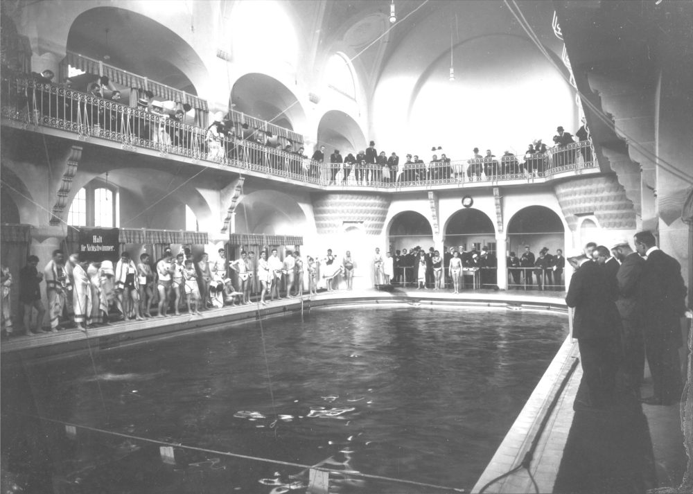 Historische Aufnahme in Schwarz-Weiß vom Volksbad Jena mit Schwimmbecken und Menschen, die um das Becken stehen.