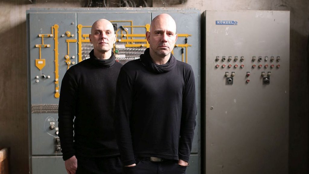Bandportrait De/Vision, beide Musiker sind schwarz gekleidet in einer alten Elektroanlage
