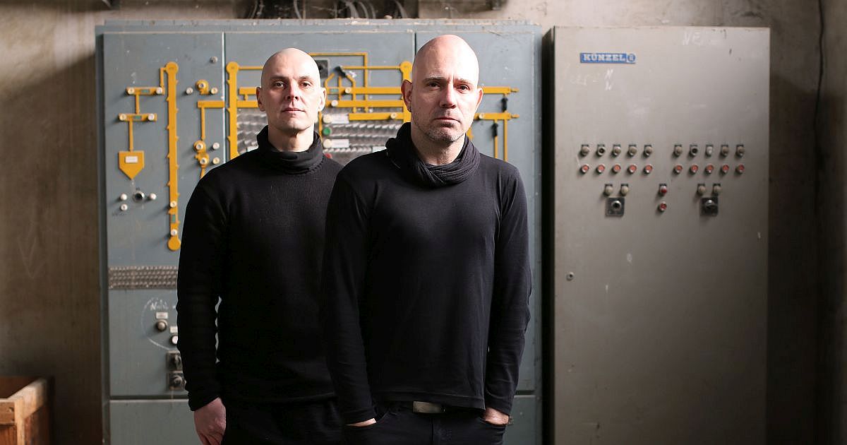 Bandportrait De/Vision, beide Musiker sind schwarz gekleidet in einer alten Elektroanlage