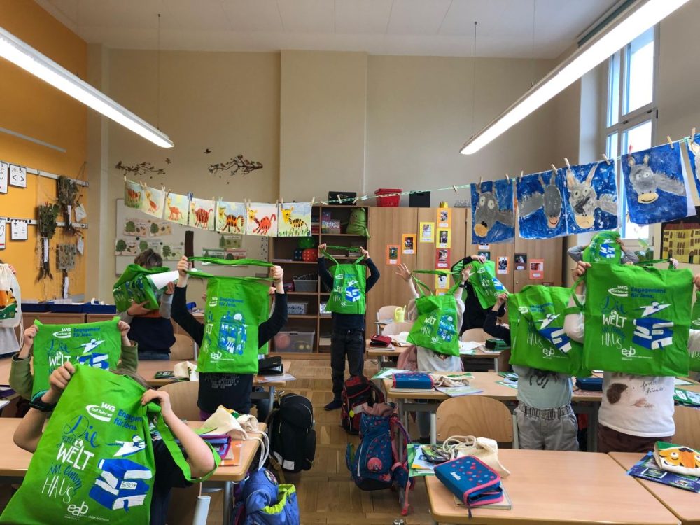 Lesetütenübergabe der EAB Jena in eienr Schulklasse, die Kinder halten die vollen Lesebeutel hoch