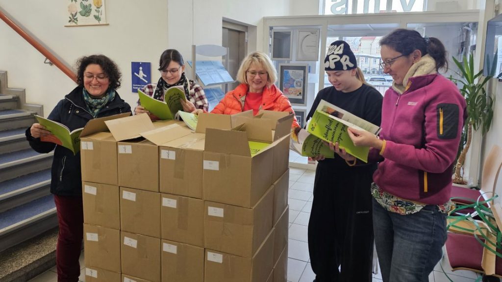 Das Team der vhs Jena steht hinter Kartons mit Programmheften und blättert in den Heften.