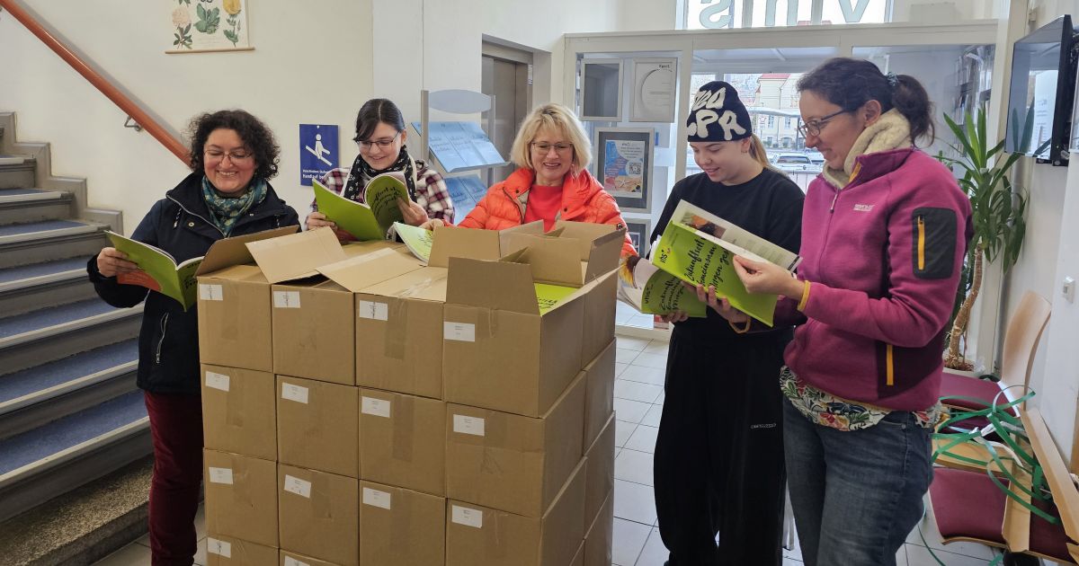Das Team der vhs Jena steht hinter Kartons mit Programmheften und blättert in den Heften.