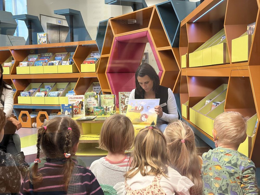 Vorlesen für KITA-Kinder in der EAB Jena: Eine EAB-Mitarbeiterin liest den lauschenden Kindern ein Bilderbuch vor