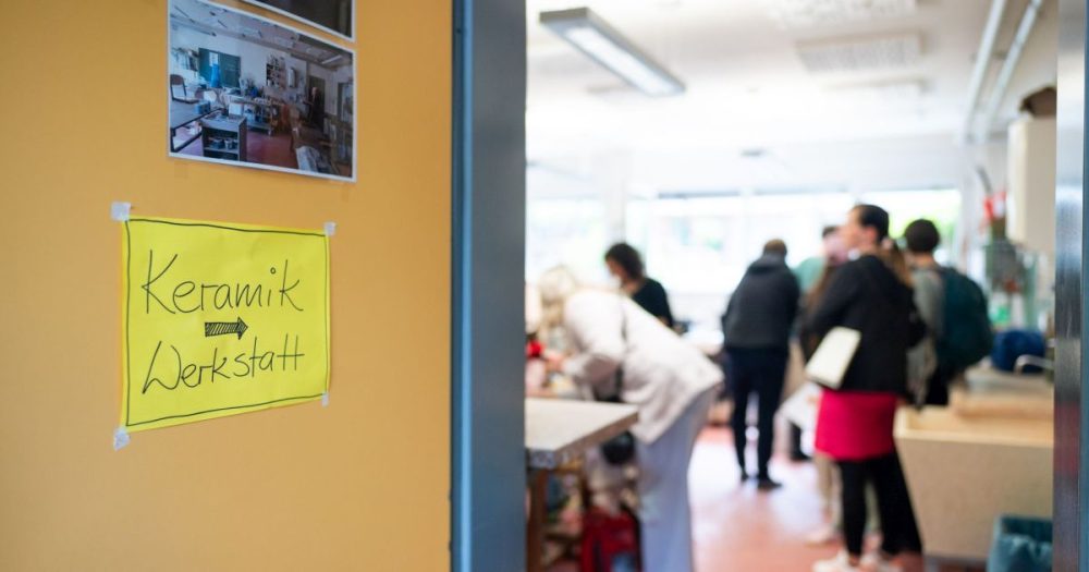 zu sehen ist der Eingang in ein Zimmer. Links ist die offenstehende Tür mit einem gelben Schild, auf dem "Keramik Werkstatt" steht und ein Pfeil Richtung Raum weist. Im Raum sieht man verschwommen einige Personen